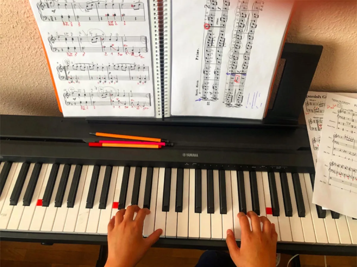 Manos de un alumno practicando piano con partituras anotadas